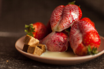 Red ripe strawberries on round plate with a few cane sugar pieces and melted white chocolate