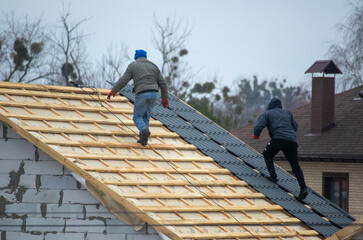 a professional roofer with electric screwdriver covers repairs the roof