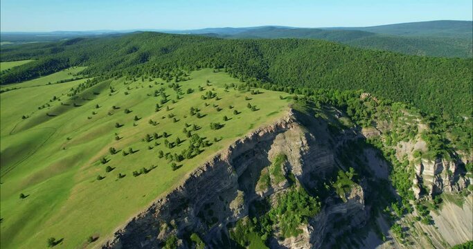 A rock with a steep rise. Dense forest and mountains on the horizon. View from the height of the mountains and forests.