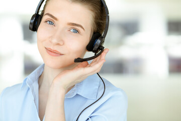 Beautiful female specialist with headphones helping customers online and smiling charmingly in modern call center office. Business people concept