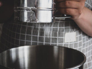 The girl's hand holds a metal sifter of flour, flour is sprinkled through a sieve. Sifting flour. Preparation for baking.