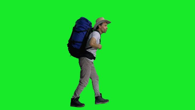 Hiker in cowboy hat with backpack walking on green screen background, Side view, chroma key 4k footage