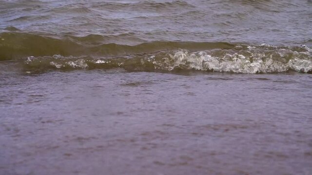 Sea coast with waves in cloudy weather close-up. Waves on the Gulf of Finland in St. Petersburg. 4K video.