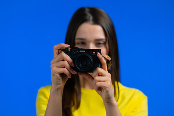 Young pretty woman takes pictures with DSLR camera over blue background in studio. Girl smiling as photographer.