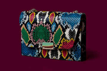 Close-up of a fashionable small handbag, a clutch, made of snakeskin. Bright colors. Dark burgundy background.