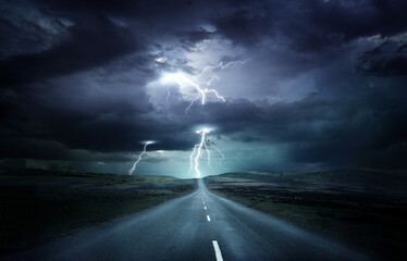 Extreme weather conditions. An empty landscape with a road leading into a powerful thunderstorm with lightning strikes. Photo composition. - obrazy, fototapety, plakaty