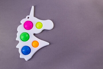 Bright colorful toy Simple Dimple in the shape of a unicorn. Popular anti stress toy on gray background, copy space