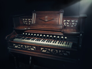 Fototapeta na wymiar Beautiful old wooden piano and black finishes along with a spotlight that illuminates its design. Retro piano, classic style. Instrumental classical music. Classic culture. Vintage, retro, obsolete.
