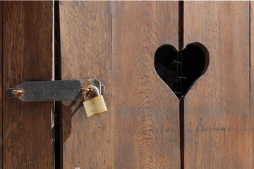 Lock-closed brown wooden door with cut hearts. Closeup