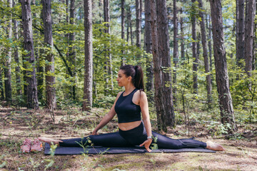 Healthy young sporty woman is making splits on a yoga mat in the forest