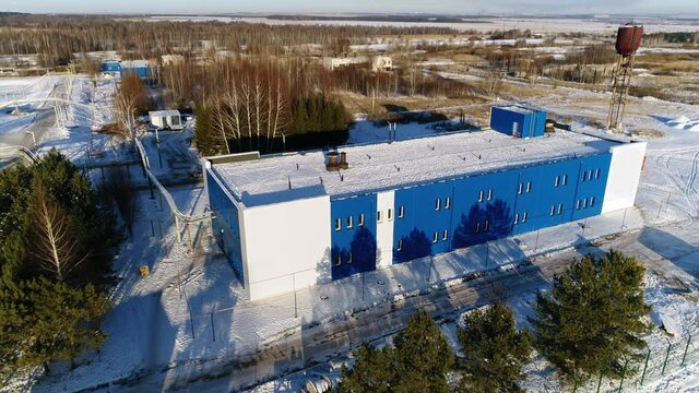 Blue and white workshop in yard of wastewater treatment plant covered with snow in winter evening bird eye view