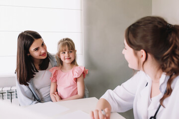 Fototapeta premium Mother or sister with small girl visiting family doctor in the clinic