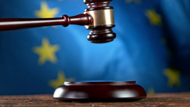 Super slow motion of gavel being struck to decide an auction or guilty verdict in court, EU flag waving on background. Filmed on high speed cinematic camera.