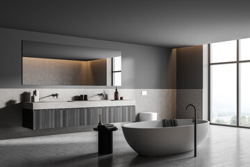 Bathtub and sink with mirror in grey concrete bathroom interior with window