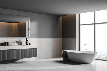 Fototapeta na wymiar Bathroom interior with bathtub near window and sink with mirror, grey floor