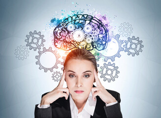 Businesswoman with pensive look, gears and colourful brain sketch on blue wall