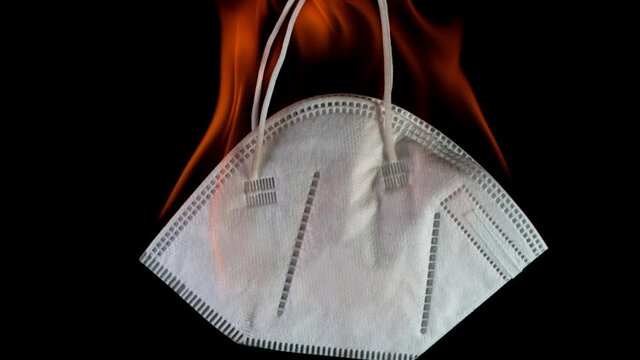 Super Slow Motion of Burning Medical Mask on Black Background. The Coronavirus is Destroyed in a Fire, End of Covid-19 Restrictions.