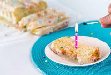 A freshly lit candle atop a slice of confetti loaf cake with a hand holding a burnt out match.