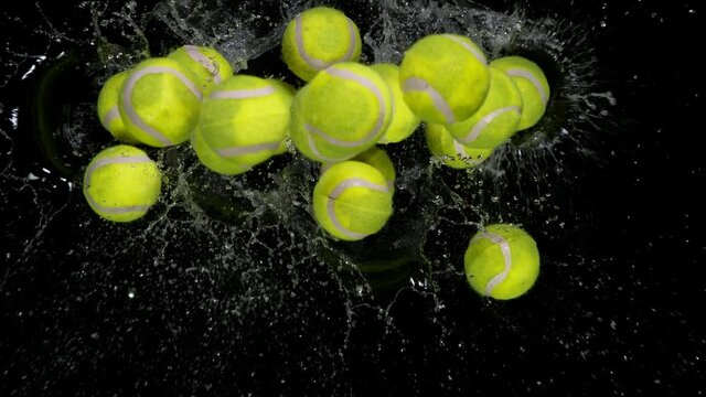 Super slow motion of falling tennis balls on water surface with water splashing during impact, black background, 1000 fps.