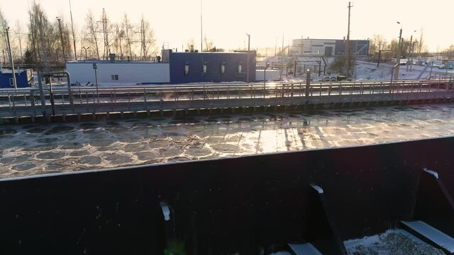 Huge tank with processed swirling dirty water at contemporary filtration station at sunset in winter evening bird eye view