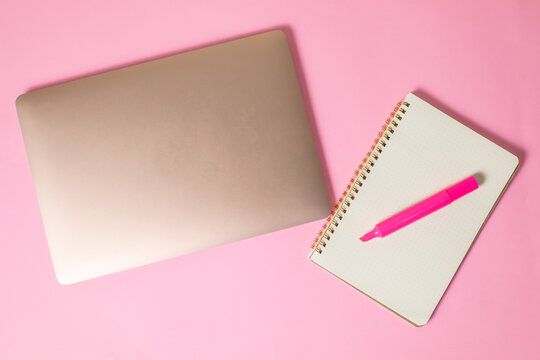 computadora junto con una libreta y un marcatextos, en fondo uniforme con todo rosa pastel
