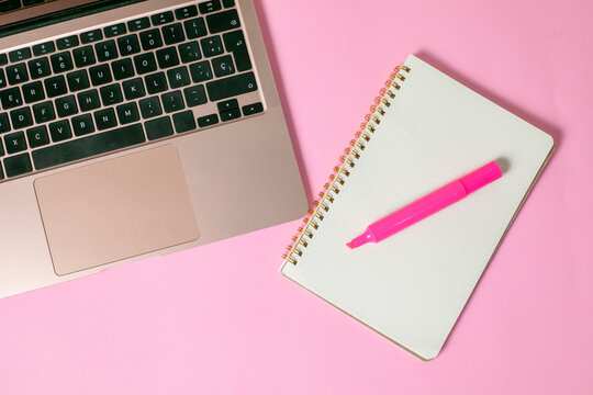 computadora junto con una libreta y un marcatextos, en fondo uniforme con todo rosa pastel