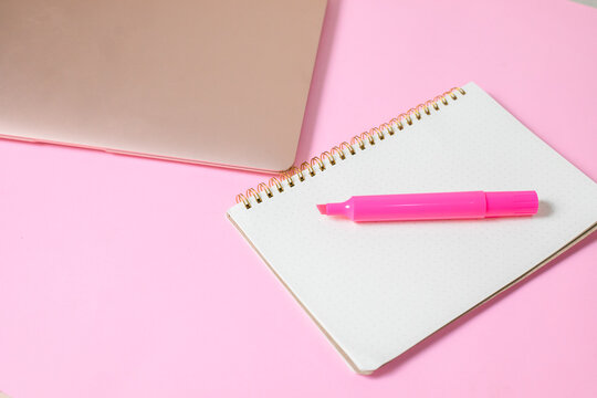 computadora junto con una libreta y un marcatextos, en fondo uniforme con todo rosa pastel