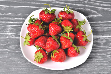 red large strawberries in a white plate on a natural grey  background close-up, selective focus