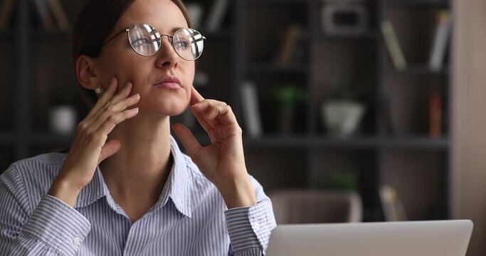 Thoughtful serious woman in glasses lost in thoughts sit near laptop. Absent-minded businesswoman think about project idea, search problem solution, looks worried pondering business strategy, close up