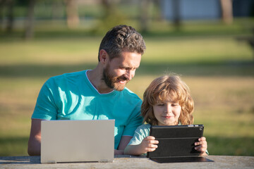 Happy father using laptop relax with schooler son holding laptop have fun together, smiling dad and little boy child enjoy weekend with gadgets outside on nature.