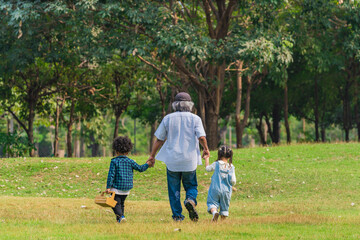 Naklejka na ściany i meble grand father holding hands of grandchildren walking together in park
