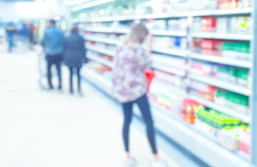 young woman near the dairy racks of supermarket, unfocused