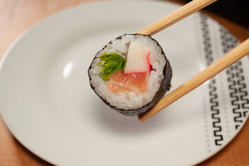A pair of chopsticks holding one sushi over a small white plate 