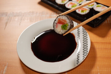 A pair of chopsticks holding one sushi over a small plate with soy sauce