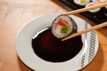 A pair of chopsticks holding one sushi over a small plate with soy sauce
