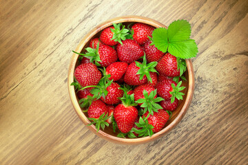 Fresh strawberries in a bowl on a wooden table. Summer food, fruit background, delicious food. Top view, copy space.