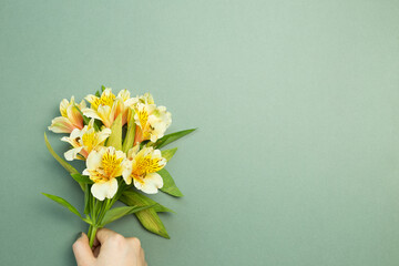 Hand holding yellow Alstroemeria flowers bouquet on green background. flat lay, top view, copy space
