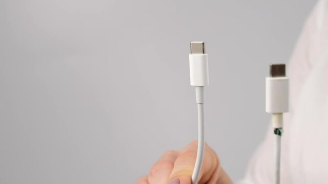 Close-up woman holding torn phone charger type-c wire.