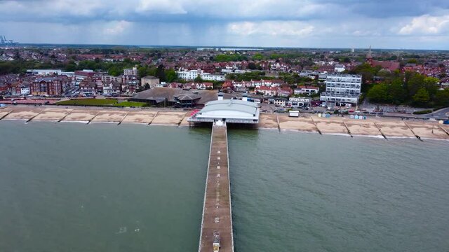 Pier and Beachfront; a revealing aerial footage of a pier and a town, communities and houses, cars moving and parking areas, birds flying below, lovely rainclouds plus rain falling in the horizon.