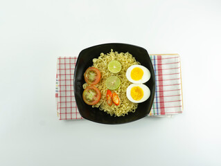 Indonesian noodle With a black bowl with eggs and fresh tomatoes on a napkin base on a white background