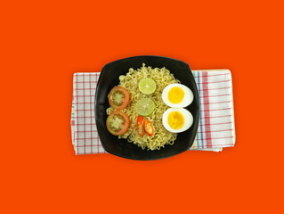 Indonesian noodle With a black bowl with eggs and fresh tomatoes on a napkin on a red background