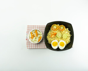 Indonesian warm noodles in a bowl and also fresh eggs and tomatoes on napkin base plus pickled cucumber in a white bowl on a white background