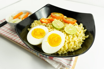 Indonesian noodle With a black bowl with eggs and fresh tomatoes on a napkin base on a white background