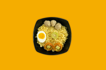 Indonesian Warm noodles served with eggs and fresh tomatoes with meatballs on a black bowl and pickled on a white bowl on a white background