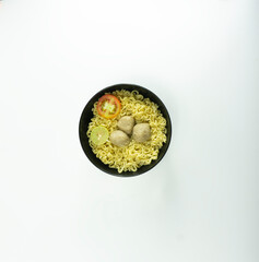 Indonesian Warm noodles served with fresh tomatoes and meatballs in a round bowl on black and pickles on a white bowl on a white background
