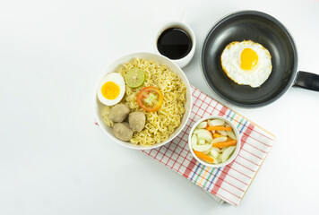 Indonesian Warm noodles served with fresh tomatoes and meatballs on a white round bowl and pickles on a white bowl on a white background