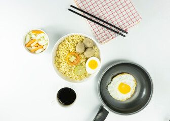 Indonesian Warm noodles served with fresh tomatoes and meatballs on a white round bowl and pickles on a white bowl on a white background