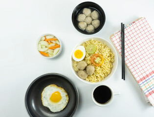 Indonesian Warm noodles served with fresh tomatoes and meatballs on a white round bowl and pickles on a white bowl on a white background