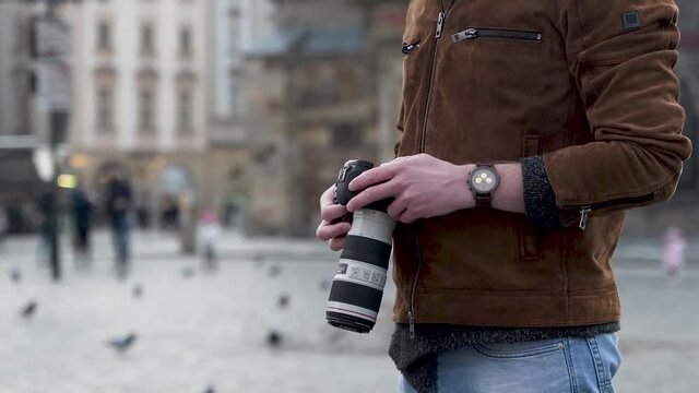 Torso of a man from the side,holding a professional camera in a city.