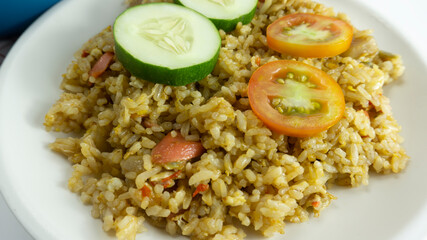 Nasi goreng or Indonesian Fried rice served with fresh tomatoes and meatballs on a white ceramic plate and pickles on a white bowl on a white background